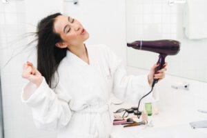 Optimistic young woman dry hair with hair dryer.